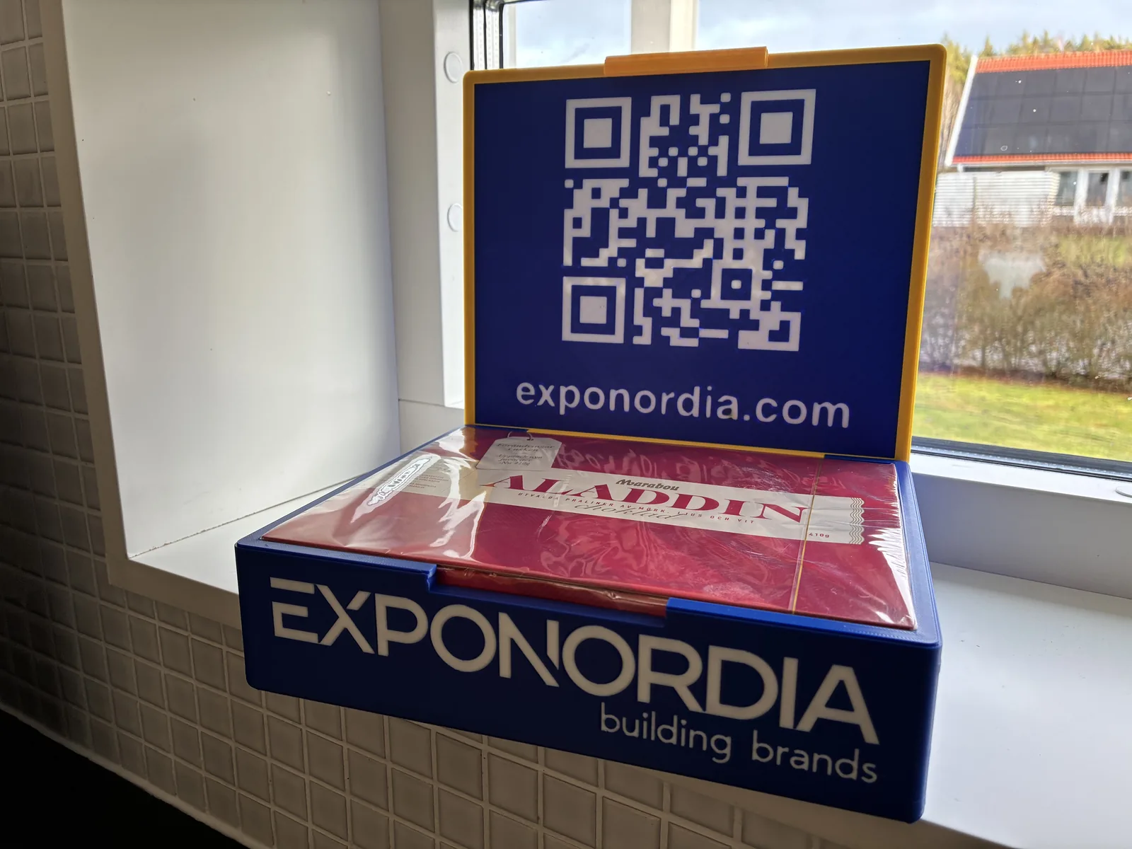 Asken öppen med QR-kod i locket och en chokladask inuti.